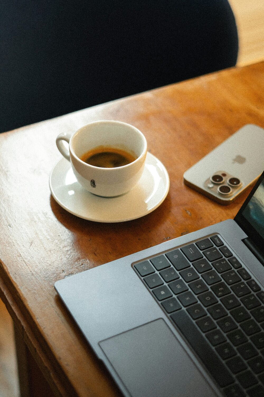 A cup of coffee on a wooden table next to a laptop